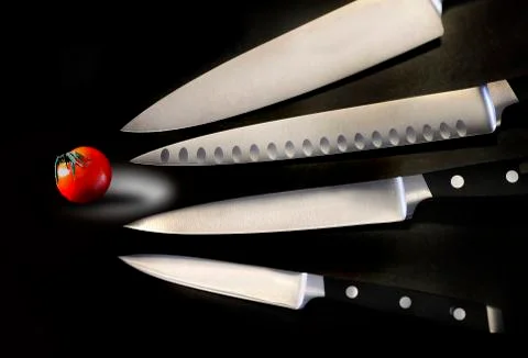 Assorted sharp and shiny kitchen knives are seen with a small tomato in this Stock Photos