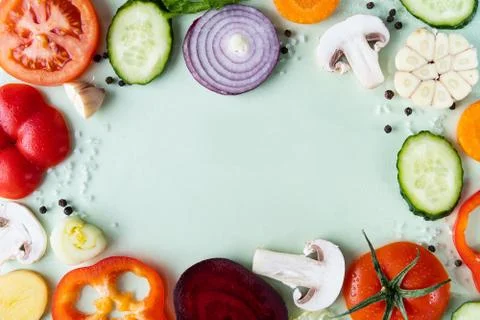 Assorted sliced vegetables on green background arranged in frame Stock Photos