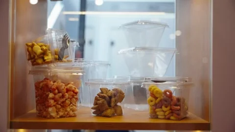 Assorted snacks displayed in clear plastic containers on a wooden shelf Stock Footage 325672026