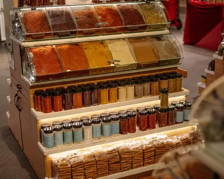 Assorted spices in open trays and small glass jars at a market stall, color.. 스톡 사진