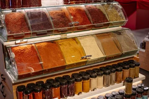 Assorted spices in open trays and small glass jars at a market stall, color.. 스톡 사진