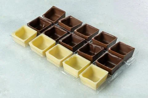 Assorted square-shaped chocolate shells inside molds. Stock Photos