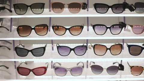 Assorted sunglasses neatly arranged on store display with reflections on lenses Vidéo 320147356