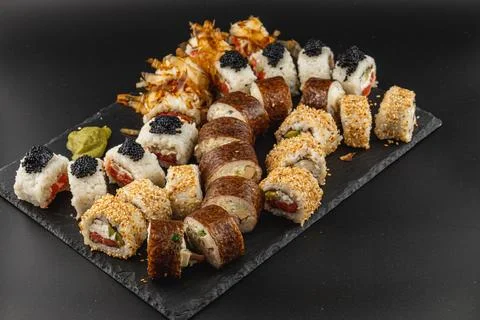 Assorted sushi platter featuring rolls and garnishes on a black tray Stock Photos