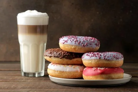 Assorted sweet donuts with icing and toppings, and coffee latte on a brown wo Foto stock