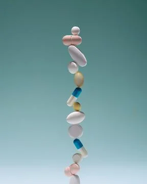 Assorted tablets and capsules form tall vertical stack on teal background, .. Fotos de archivo