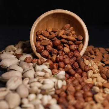 Assorted types of nuts scattering from wooden bowl 스톡 사진