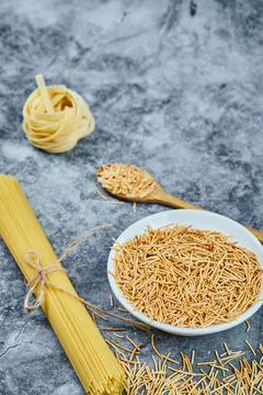 Assorted uncooked pasta on a marble background with a wooden spoon Stock Photos