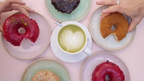 Assorted vegan doughnuts served around cup of matcha latte on pastel pink table Stock Footage 139533680