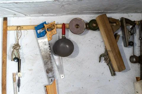 Assorted vintage carpentry tools hang on a rustic white wall in a workshop, Stock Photos