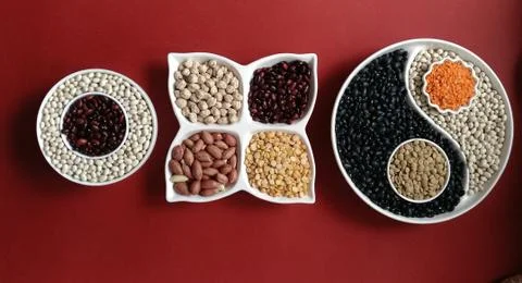 Assortment of beans in containers of different shapes on a red background. to Stock Photos