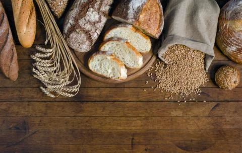Assortment of bread, ears and grains of wheat on wooden table Stock Photos
