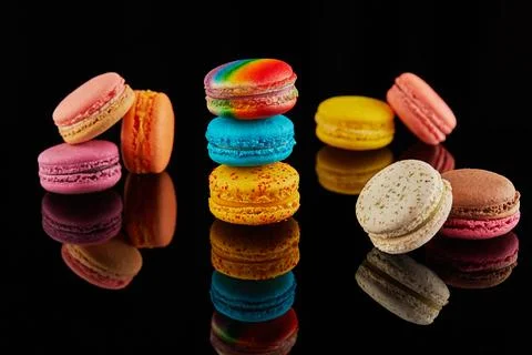An assortment of bright macarons of different colors lies on a black backgrou Stock Photos