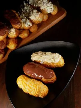 Assortment of eclairs with chocolate icing. Sweets on a triangular black plate. Stock Photos
