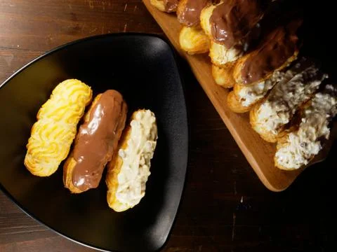 Assortment of eclairs with chocolate icing. Sweets on a triangular black plate. Stock Photos