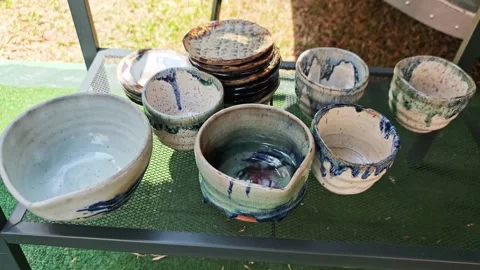 Assortment of handmade ceramic cups, bowls, and saucers on a shelf. Video stock 340506822
