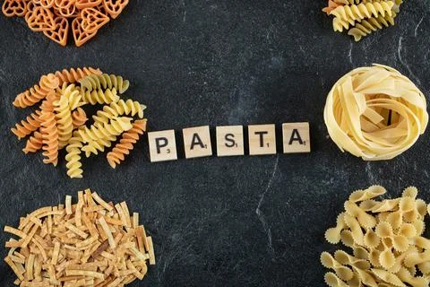 Assortment of raw pasta on dark background with wooden letters Stock Photos