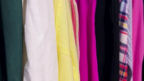 Assortment of shirts and blouses in different colors hang on hangers. Stock Footage 311945568