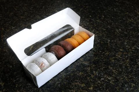 An assortment of various donuts in a white box on a countertop. Stock Photos