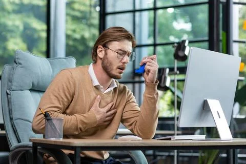 Asthma attack, panic attack. A young man sits in the office at the table, holds Foto stock