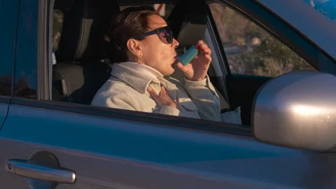 Asthmatic woman using an inhaler while driving her car 库存影片 329284213