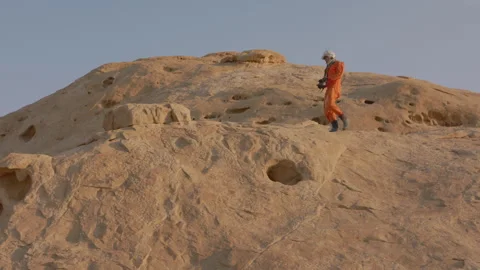 Astronaut exploring unique rock formations in a desert landscape at sunset Stock Footage 288671868