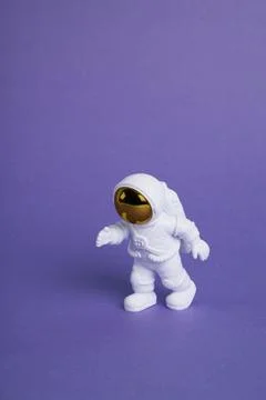An astronaut figurine in a spacesuit exploring a plain purple background Stock Photos