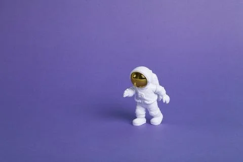 An astronaut figurine in a spacesuit exploring a plain purple background Stock Photos