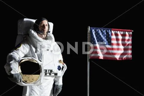 An astronaut holding his helmet standing next to an American flag, portrait Stock Photos