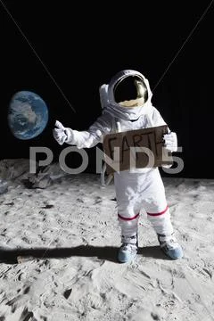 An astronaut on the moon with his thumb out, holding 'EARTH' sign Stock Photos