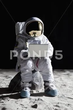 An astronaut on the moon sitting on a rock using a laptop Stock Photos