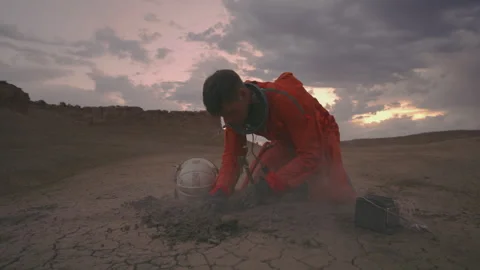 Astronaut in orange suit exploring desert landscape at sunset Stock Footage 288799725