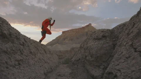 Astronaut performs jumps across desert terrain with stunning mountain backdrop Stock Footage 288676987