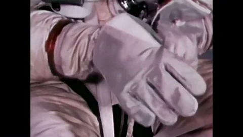 An astronaut pulling on a glove, showing his spacesuit, a handler helping him to Stock Footage 85203381