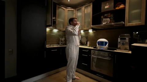 An astronaut rests in his kitchen and drinks water Stock Footage 220103247