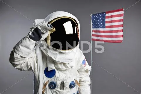 An astronaut saluting next to an American flag, studio shot Stock Photos
