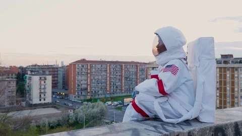 Astronaut sitting on wall looking over city Stock Footage 154792354