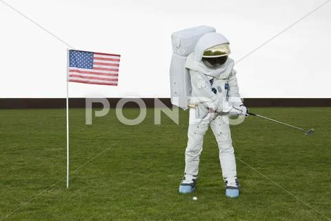 An astronaut swinging a golf club next to an American flag Stock-Fotos