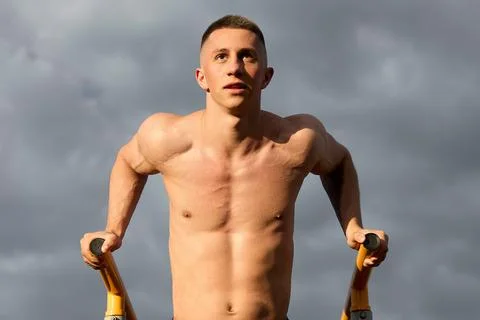 Athlete with a bare torso hangs on parallel bars, push-ups, muscles are tense Stock Photos