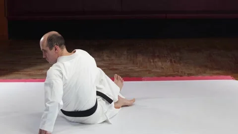 An athlete with a black belt performs a back stretch while sitting on the floor Stock Footage 272741161