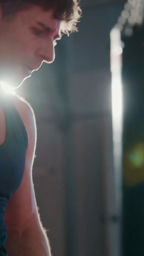 Athlete in dark tank top strained during exercise, light behind him Stock Footage 335506548