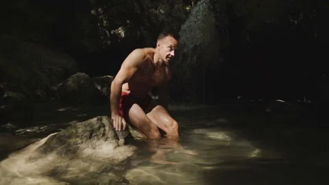 Athlete doing exercise, standing in a beautiful mountain waterfall. Travel Stock Footage 94937824