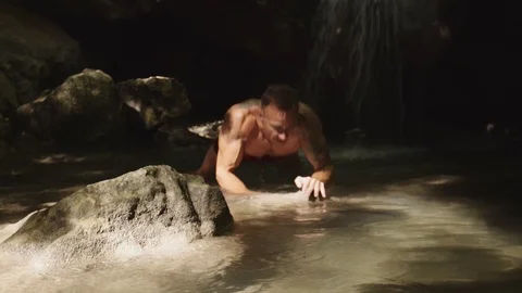 Athlete doing exercise, standing in a beautiful mountain waterfall. Nature Stock Footage 94937826