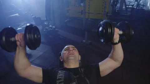 An athlete is doing a workout with dumbbells. Man trains muscular arms. Video stock 234179184