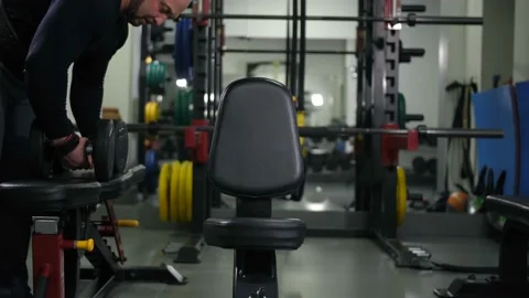 The athlete with dumbbells sits on a bench, does an exercise for two hands 4K Video stock 100260383