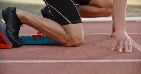 An athlete is getting ready for sprinting, putting feet in starting blocks, then Stock Footage