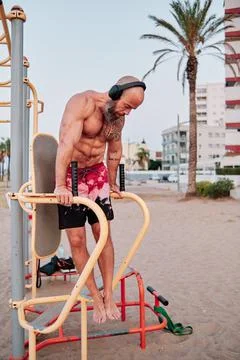 Athlete man exercising on parallel bars outdoors at the beach. Stock Photos