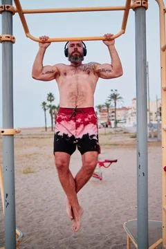Athlete man practicing calisthenics while doing pull-ups outdoors at the beach. Stock Photos