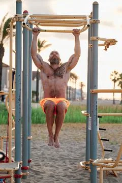 Athlete man practicing calisthenics while doing pull-ups on the bar outdoors at Stock Photos