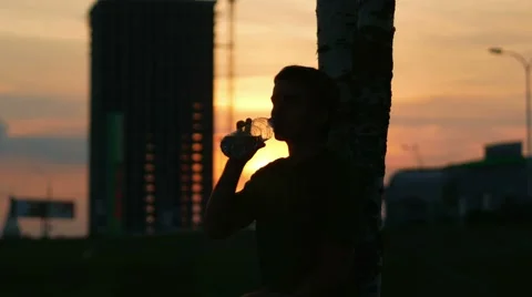 Athlete man resting at sunset and drinks water from a bottle. Sun beautifully Stock Footage 66454745
